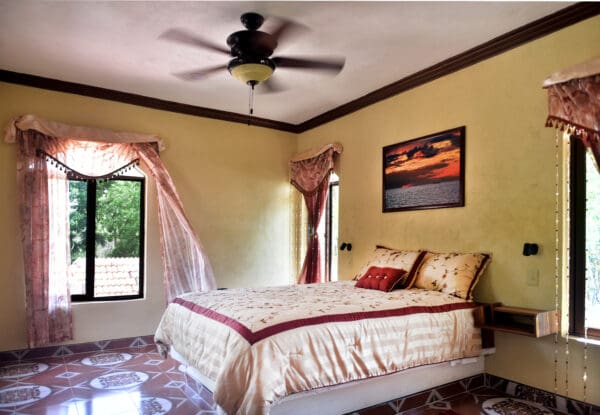 A bedroom with a bed, ceiling fan and window.