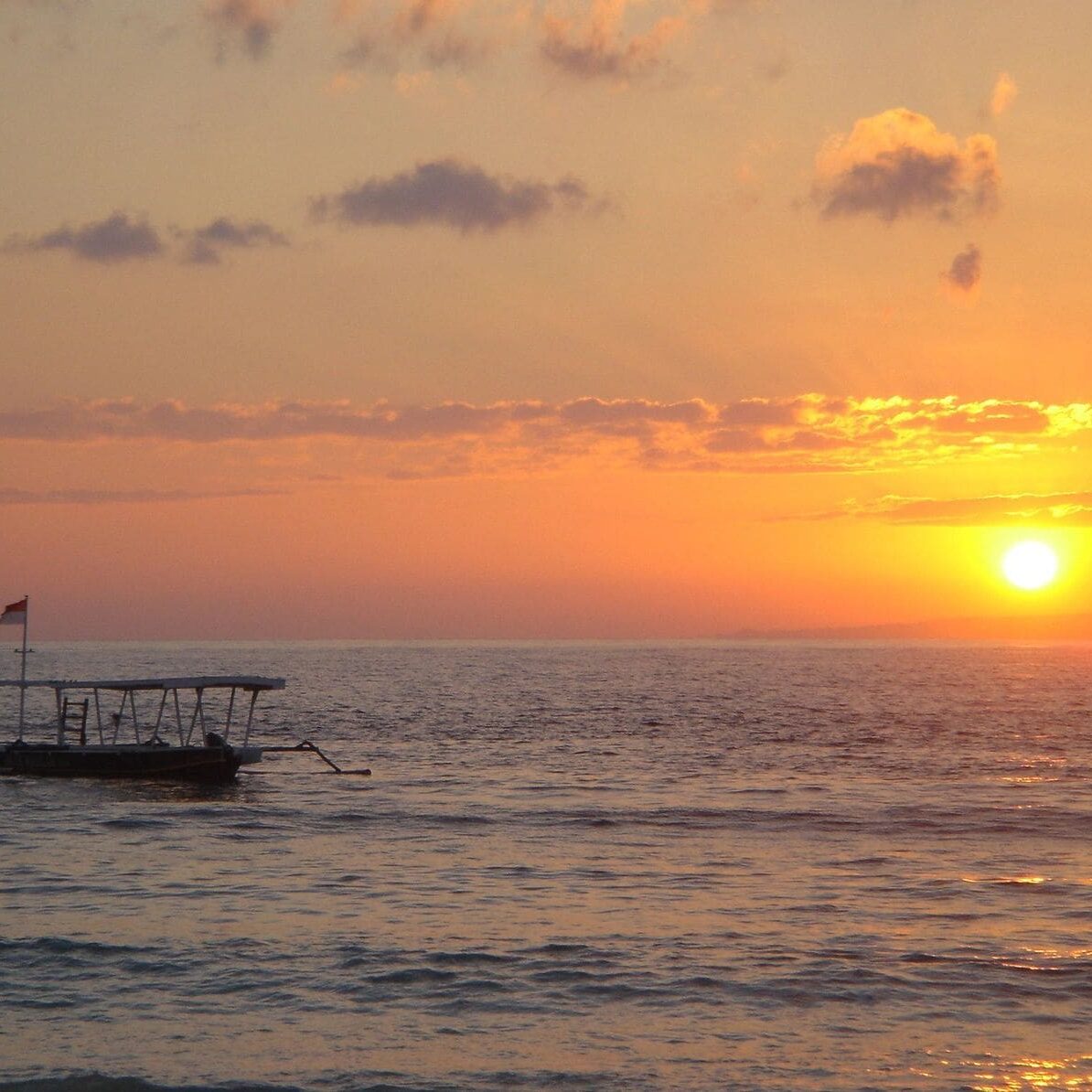 A boat is in the ocean at sunset.